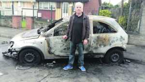 Sinn Fein councillor John Costelloe with a burnt out  car on Quarry Road.