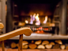 Home comfort. Rocking chair near the fireplace. Photo of interior of room. Rocking chair in the living room with decorated modern fireplace