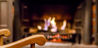 Home comfort. Rocking chair near the fireplace. Photo of interior of room. Rocking chair in the living room with decorated modern fireplace