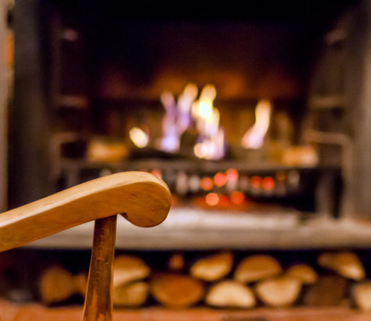 Home comfort. Rocking chair near the fireplace. Photo of interior of room. Rocking chair in the living room with decorated modern fireplace