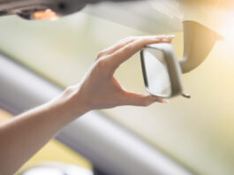 Young woman adjusting a rear-view mirror in the car