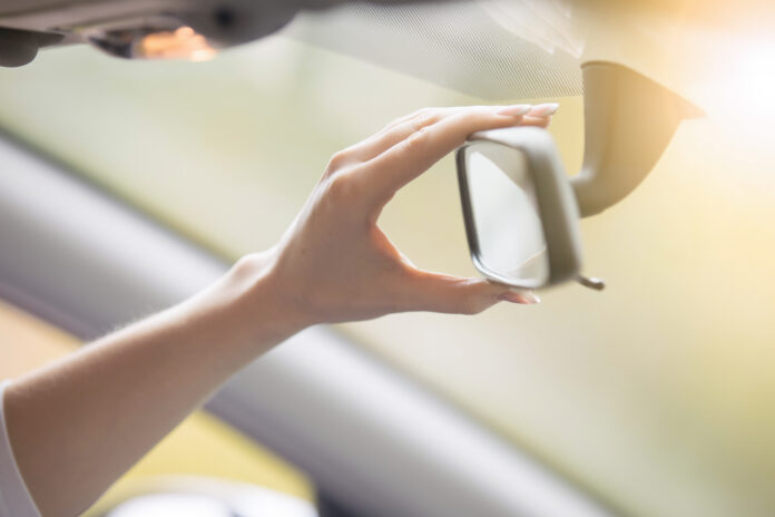 Young woman adjusting a rear-view mirror in the car