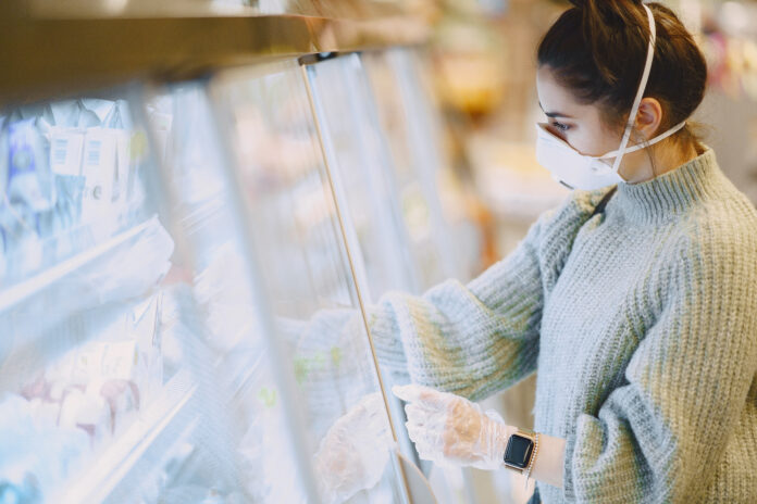 Woman in a supermarket. Lady in a respirator. Girl makes parchases.