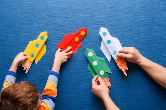 Father and little son are playing with rocket made of paper in the home. Cheerful time together at home. preschool Child in creativity in the home.