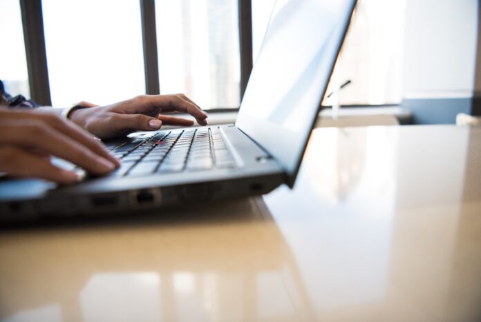 person using black laptop on brown table