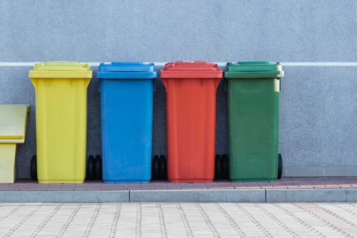 four assorted-color trash bins beside gray wall