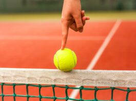 person holding yellow tennis ball on red and white net