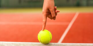 person holding yellow tennis ball on red and white net