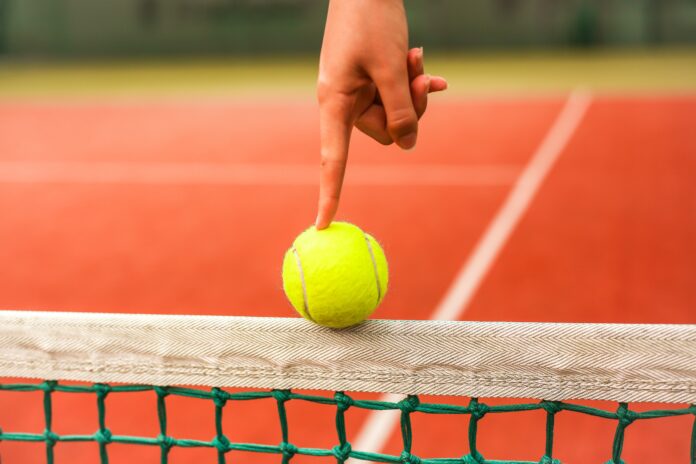 person holding yellow tennis ball on red and white net