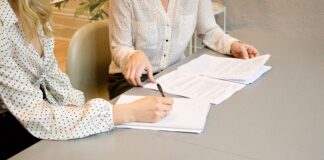 woman signing on white printer paper beside woman about to touch the documents