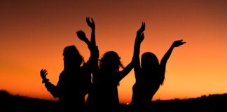 silhouette of three woman with hands on the air while dancing during sunset