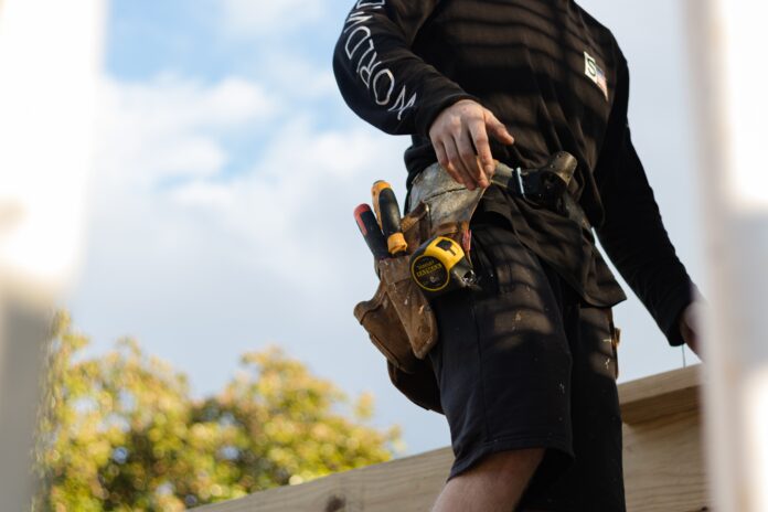 person in black leather jacket holding brown and black hiking shoes