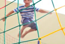 boy in blue and white striped shirt climbing on yellow metal fence